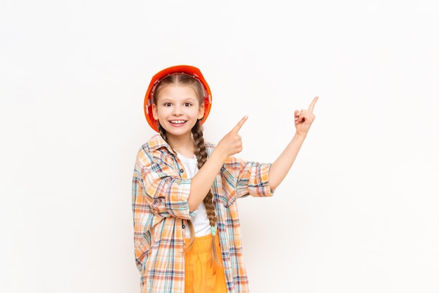 Ein junges Mädchen in einem schützenden Bauhelm zeigt auf einem weißen, isolierten Hintergrund auf Ihre Werbung Ein Kind in einem karierten Hemd bereitet sich auf Reparaturarbeiten vor