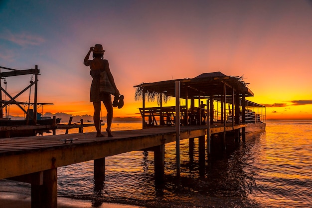 Ein junges Mädchen in einem Sonnenuntergang auf einem Pier an einem Strand auf der Insel Roatan, Honduras