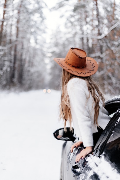 Ein junges Mädchen in einem Winterwald zwischen der Straße im Auto schaut in die Ferne