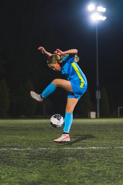 Ein junges Mädchen in einer blauen Uniform spielt mit einem Ball bei einem Sportler-Kinder-Konzept.