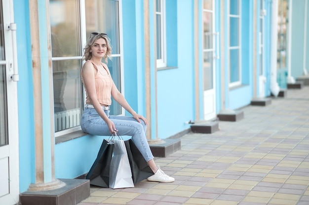 Foto ein junges mädchen in jeans mit taschen sitzt im sommer auf der straße in der nähe des ladens