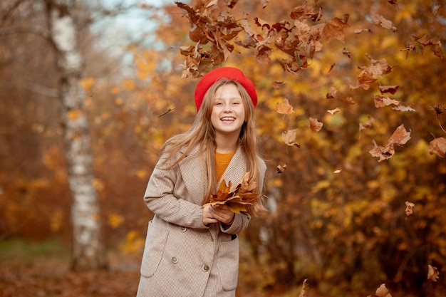 Ein junges Mädchen in roter Baskenmütze und Mantel hält einen Strauß Herbstlaub freut sich im Herbst