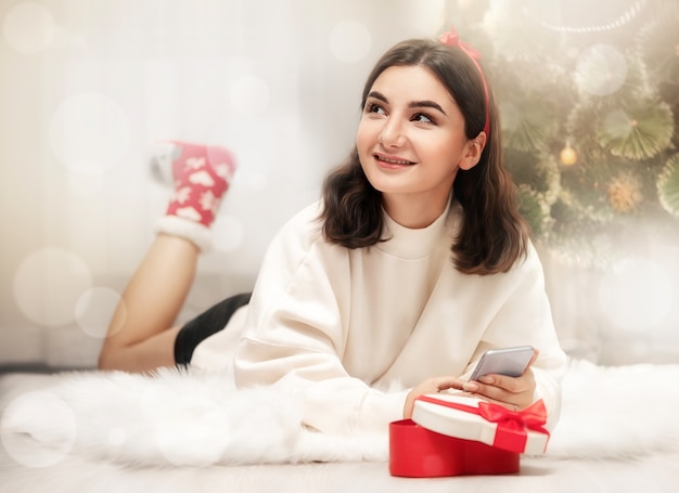 Ein junges Mädchen liegt am Weihnachtsbaum und hält ein Geschenk in den Händen