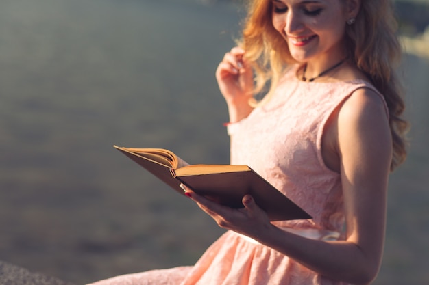 Ein junges Mädchen liest ein Buch am Ufer des Flusses.