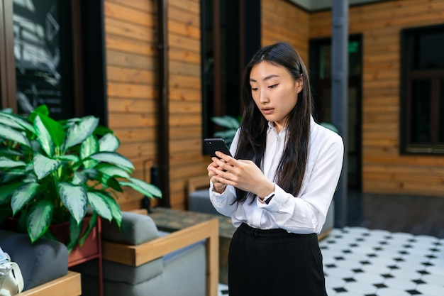 Ein junges Mädchen mit asiatischem Aussehen steht im Flur und schaut in ein Handy