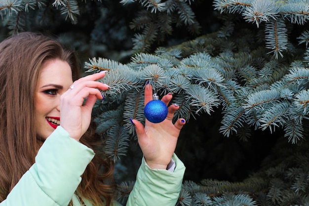 Ein junges Mädchen mit blonden Locken mit brillantem Make-up, das ein Weihnachtsspielzeug hält.