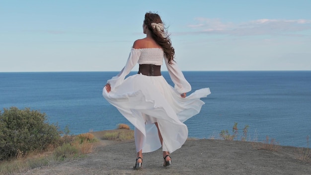 Ein junges Mädchen mit dunklem Haar in einem weißen Kleid dreht sich auf dem Gipfel des Berges, der Wind weht ihr Haar und Kleid und lächelt Harmonie Abenteuer Freiheit 4k Video Zeitlupe