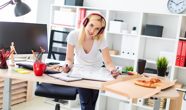 Ein junges Mädchen mit Kopfhörern steht neben dem Tisch und hält einen Stift in der Hand.