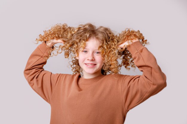 Ein junges mädchen mit lockigem haar lächelt und versucht es auf einem weißen hintergrund