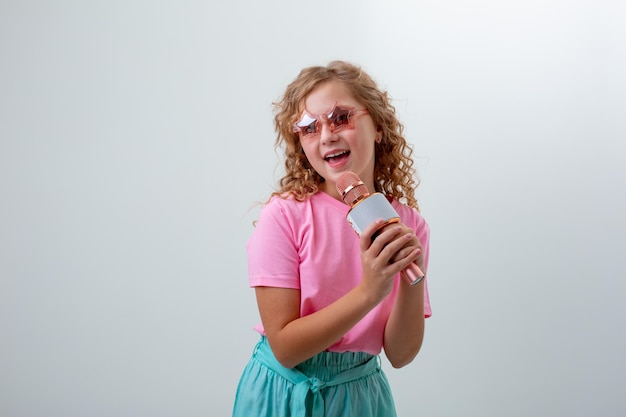 Ein junges Mädchen mit Sonnenbrille hält ein Mikrofon und singt ein Lied auf weißem Hintergrund