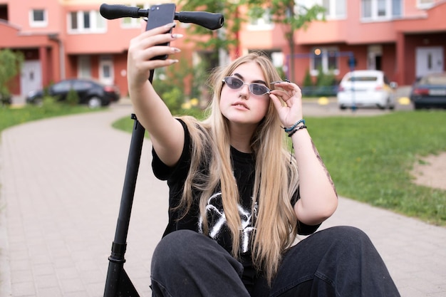 Ein junges Mädchen mit Sonnenbrille macht ein Selfie auf einem Roller