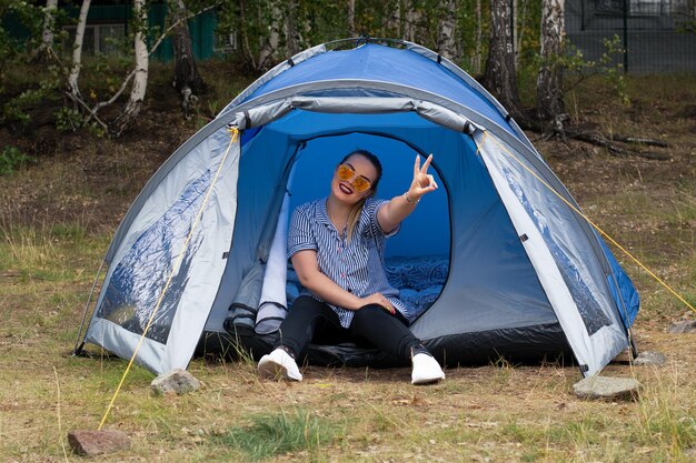 Ein junges Mädchen mit Sonnenbrille sitzt in einem Zelt in der Natur