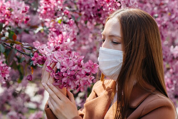 Ein junges Mädchen nimmt die Maske ab und atmet nach dem Ende der Pandemie an einem sonnigen Frühlingstag vor blühenden Gärten tief durch. Schutz und Prävention 19.