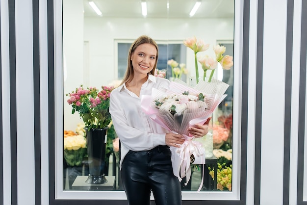 Ein junges Mädchen posiert mit einem schönen festlichen Blumenstrauß vor dem Hintergrund eines gemütlichen Blumenladens Floristik und Blumenstraußherstellung in einem Blumenladen Kleines Unternehmen