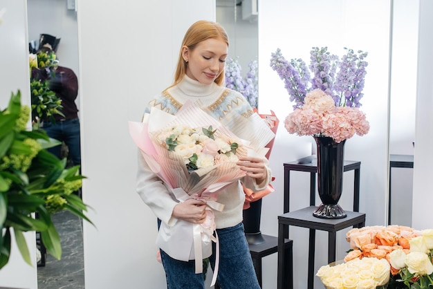 Ein junges Mädchen posiert mit einem schönen festlichen Blumenstrauß vor dem Hintergrund eines gemütlichen Blumenladens Floristik und Blumenstraußherstellung in einem Blumenladen Kleines Unternehmen