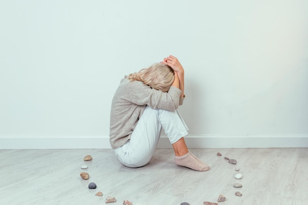 Ein junges Mädchen sitzt auf dem Boden, umgeben von einem Steinkreis. Visualisierung von Depressionen.