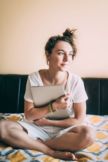 Ein junges Mädchen sitzt auf einem Bett und umarmt ihren Laptop. Digitalisierung.