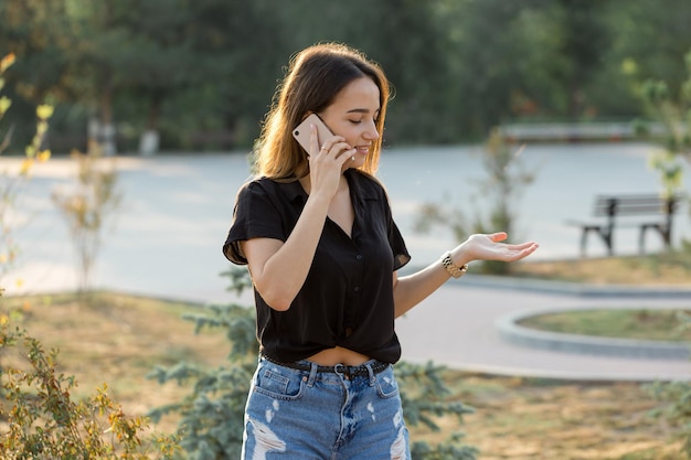 Ein junges Mädchen sitzt auf einer Bank in einem Park und macht sich Notizen In einem freien Stil gekleidet Geschäftsfrau, die am Telefon mit Kunden spricht