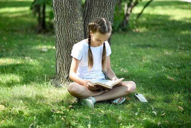 Ein junges Mädchen sitzt auf grünem Gras und liest ein Buch. Ausbildung. Kindheit.