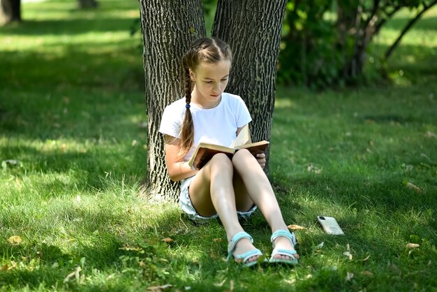 Ein junges Mädchen sitzt auf grünem Gras und liest ein Buch Bildung Kindheit