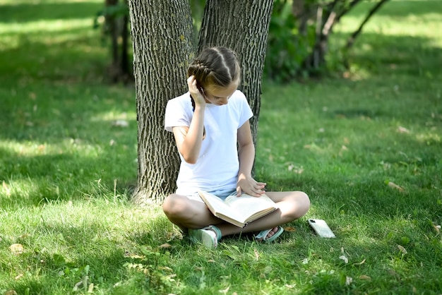 Ein junges Mädchen sitzt auf grünem Gras und liest ein Buch Bildung Kindheit