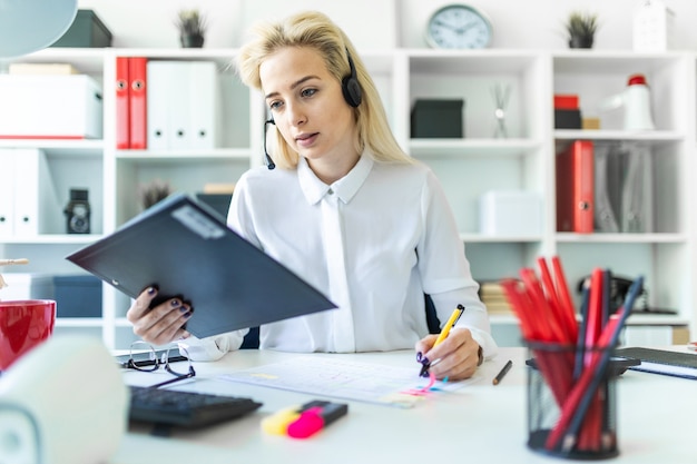 Ein junges Mädchen sitzt im Kopfhörer mit Mikrofon am Schreibtisch im Büro und macht sich Notizen im Dokument.