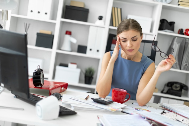 Ein junges Mädchen sitzt in ihrem Büro an einem Tisch und hält eine Brille in der Hand.