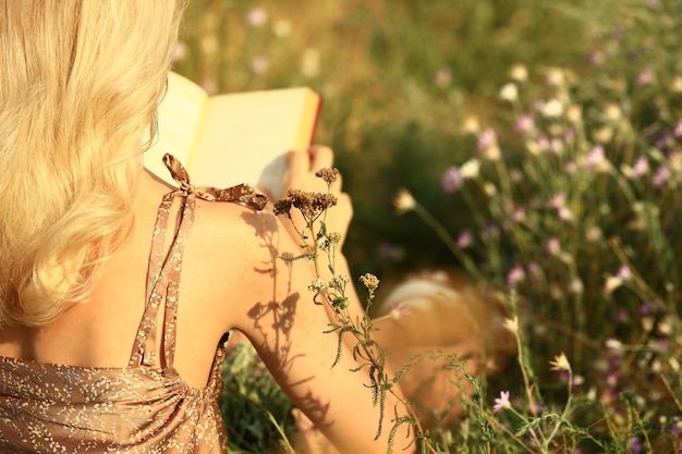 Ein junges Mädchen sitzt mit dem Rücken zur Kamera und liest ein Buch in einem Feld von Wildblumen. Sommer-Herbst-Konzept