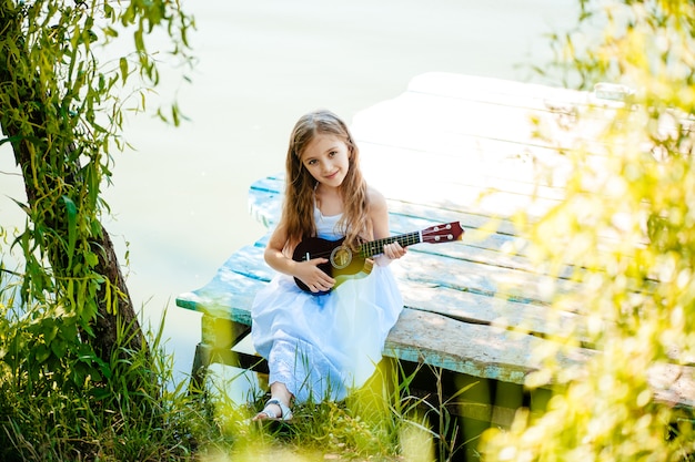 Ein junges Mädchen spielt Ukulele im Badeurlaub. Frauen liegen am tropischen Strand mit Strohhut.