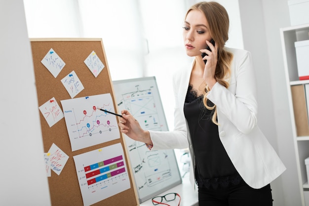 Ein junges Mädchen steht in der Nähe des Brettes mit Aufklebern, spricht am Telefon und hält einen Bleistift in der Hand.