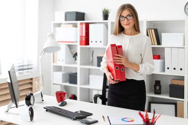 Ein junges Mädchen steht in der Nähe eines Tisches im Büro und hält einen Ordner mit Dokumenten.