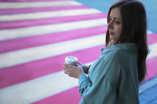 Ein junges Mädchen steht mit einer Tasse Kaffee in der Nähe eines Fußgängerüberwegs
