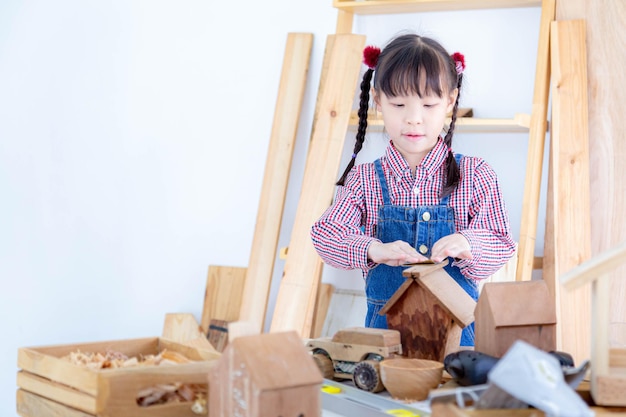 Ein junges Mädchen stellt in einer Holzfabrik ein Spielzeug in Form eines Holzhauses her.