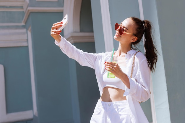 Ein junges Mädchen trinkt einen erfrischenden Sommercocktail in der Stadt und macht ein Selfie