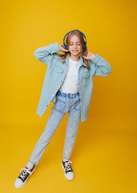 Ein junges Mädchen von 1113 Jahren mit Kopfhörern hört Musik und tanzt im Studio auf gelbem Hintergrund