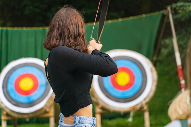 Ein junges Mädchen zielt von hinten mit einem Bogen auf ein Zielfoto. Hochwertiges Foto