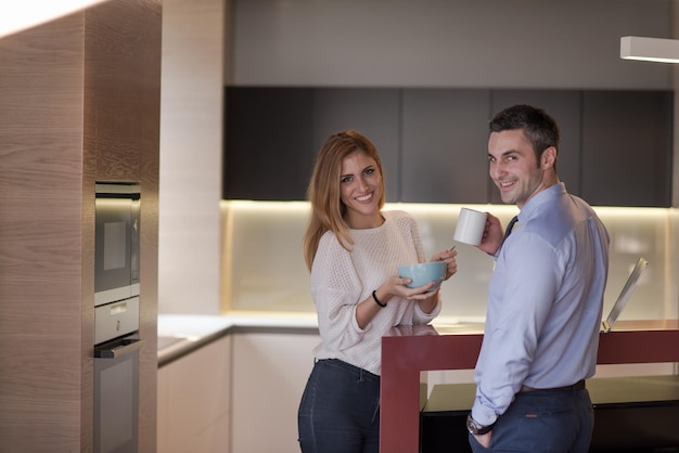 Ein junges Paar bereitet sich auf den Job vor und benutzt einen Laptop. Der Mann trinkt Kaffee, während die Frau gemeinsam in einem Luxushaus frühstückt, lächelnd auf den Bildschirm schaut.