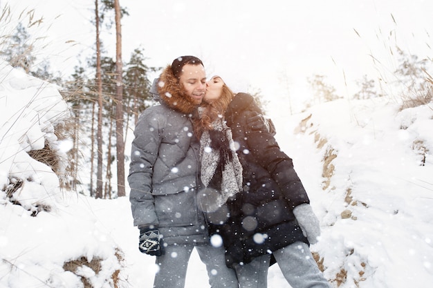 Ein junges Paar, ein Mann und eine Frau gehen in einem verschneiten Winterwald spazieren.