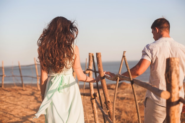 Ein junges Paar geht im Sommer an einer Hecke am Meer entlang