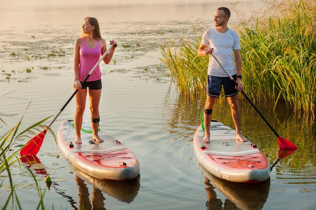 Ein junges Paar läuft auf einem aufblasbaren SUP-Brett am Fluss entlang