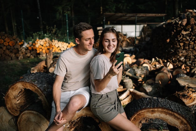 Foto ein junges paar sitzt auf gefällten bäumen im wald und schaut auf sein handy