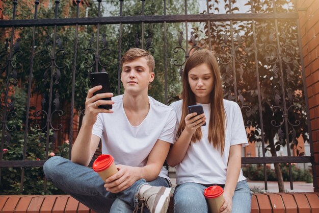 Ein junges Paar trinkt Kaffee aus Pappbechern und schaut auf Smartphones.