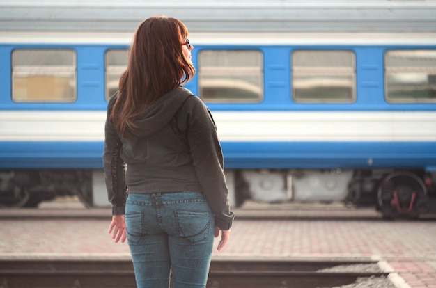 Ein junges rothaariges Mädchen steht auf dem Bahnsteig und beobachtet den abfahrenden Zug