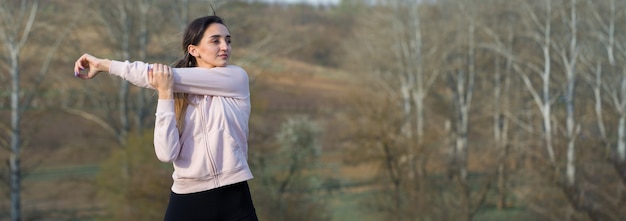 Ein junges schlankes athletisches Mädchen in Sportbekleidung führt eine Reihe von Übungen durch. Fitness und gesunder Lebensstil vor dem Hintergrund grüner Frühlingsweiden.