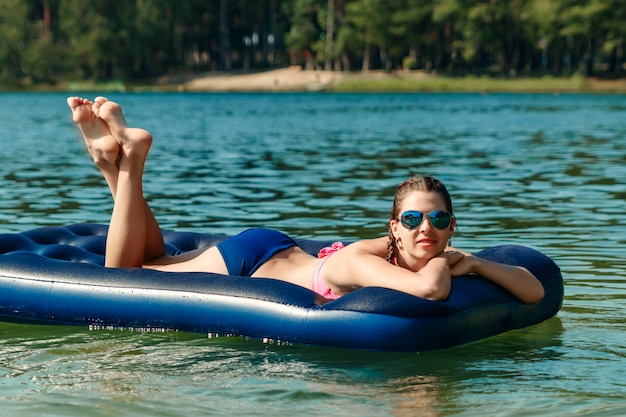 Ein junges, schönes Mädchen in Badeanzug und Sonnenbrille liegt auf einer blauen Wassermatratze gegen das Meer. Die von Urlaub, Ferien, Sommer, Ferien, Reisen. copyspace.