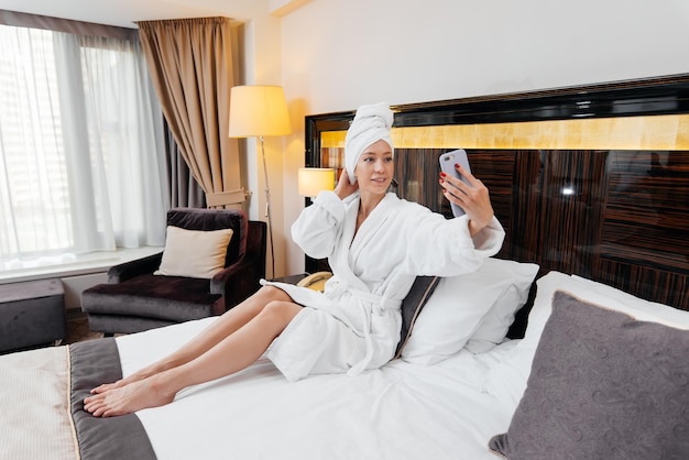 Ein junges schönes Mädchen in einem weißen Mantel telefoniert in ihrem Hotelzimmer Erholung und Reisen Erholung und Tourismus im Hotel