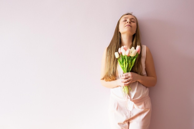 Ein junges schönes Mädchen mit blonden, aufgelösten langen Haaren und einem Filzhut auf dem Kopf hält Frühlingsblumen