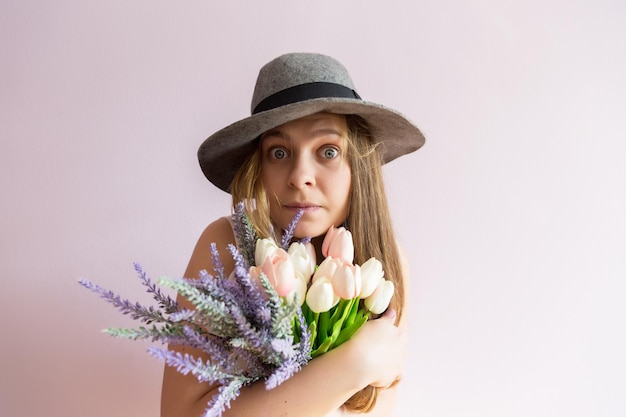 Ein junges schönes Mädchen mit blonden, aufgelösten langen Haaren und einem Filzhut auf dem Kopf hält Frühlingsblumen