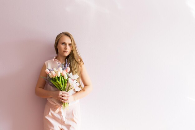 Ein junges schönes Mädchen mit blonden, langen, lockeren Haaren hält Frühlingsblumen in den Händen