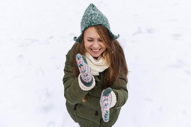 Ein junges schönes Mädchen mit langen blonden Haaren genießt den ersten Schnee Grüne Jacke, grüner Hut und Handschuhe